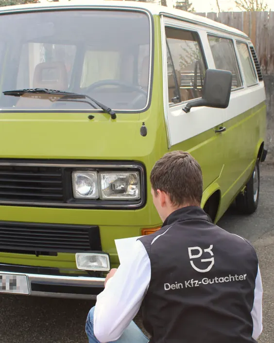 Sebastian Wyczisk kniet mit Klemmbrett vor einem grünen Oldtimer-Bus