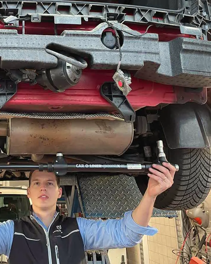 Sebastian Wyczisk hält unter der Hebebühne eine Car-O-Liner-Messbrücke an den Unterboden eines Unfallautos