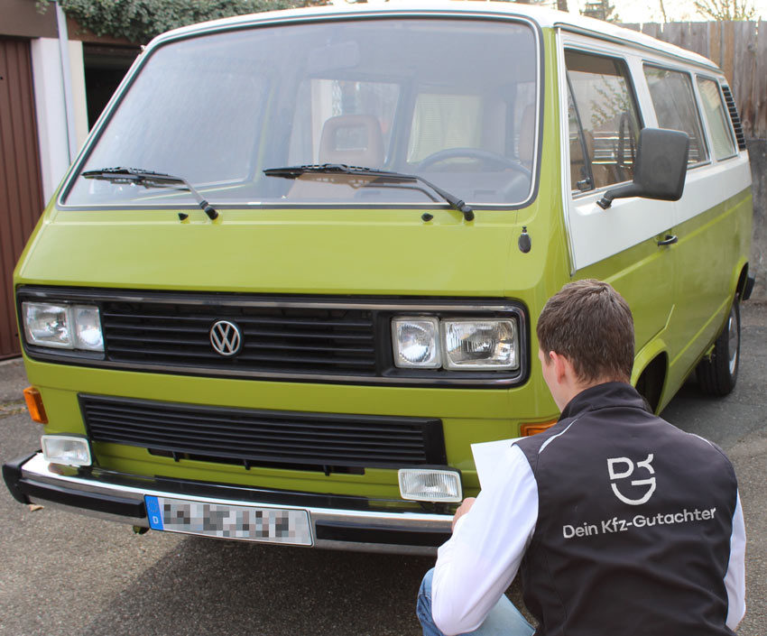 Sebastian Wyczisk kniet mit Klemmbrett vor einem grünen VW T3 Bus und begutachtet die Front